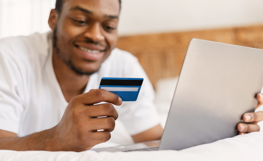 black man doing online shopping lying in bed at ho F3QMY8S